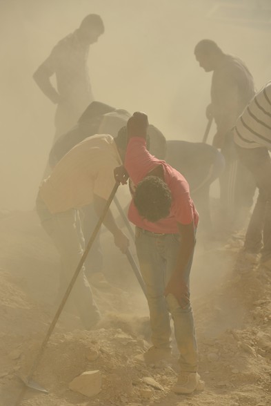Egipscy robotnicy w tumanach pyłu usuwają skalny rumosz i trap z półki skalnej,