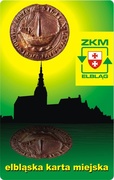 Projekt nr 1
Historyczna pieczęć elbląska z kogą „świeci” nad zarysem starówki. Odbicie pieczęci w wodzie symbolizuje kanał elbląski. Kolorystyka projektu nawiązuje do logo ZKM w Elblągu.